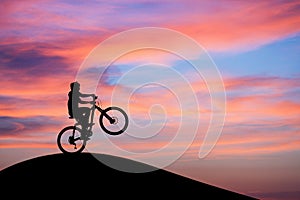 Mountainbiker doing wheelie in sunset sky on hill