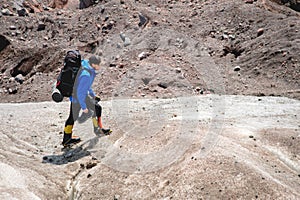 A mountaineer with a backpack walks in crampons walking along a dusty glacier with sidewalks in the hands between cracks