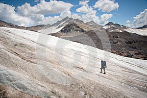 A mountaineer with a backpack walks in crampons walking along a dusty glacier with sidewalks in the hands between cracks