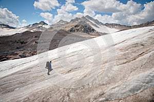 A mountaineer with a backpack walks in crampons walking along a dusty glacier with sidewalks in the hands between cracks