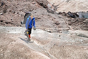 A mountaineer with a backpack walks in crampons walking along a dusty glacier with sidewalks in the hands between cracks