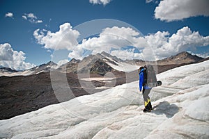 A mountaineer with a backpack walks in crampons walking along a dusty glacier with sidewalks in the hands between cracks