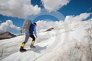 A mountaineer with a backpack walks in crampons walking along a dusty glacier with sidewalks in the hands between cracks