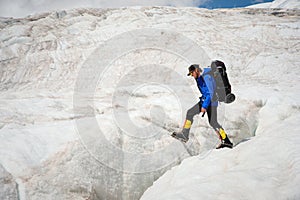 A mountaineer with a backpack walks in crampons walking along a dusty glacier with sidewalks in the hands between cracks