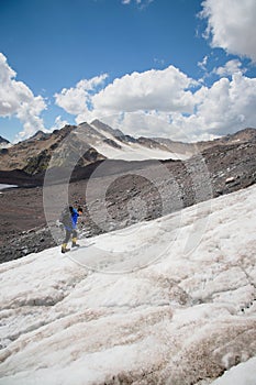 A mountaineer with a backpack walks in crampons walking along a dusty glacier with sidewalks in the hands between cracks