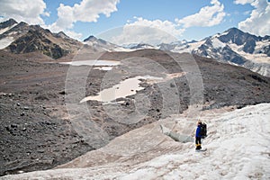 A mountaineer with a backpack walks in crampons walking along a dusty glacier with sidewalks in the hands between cracks