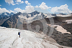 A mountaineer with a backpack walks in crampons walking along a dusty glacier with sidewalks in the hands between cracks