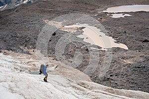 A mountaineer with a backpack walks in crampons walking along a dusty glacier with sidewalks in the hands between cracks