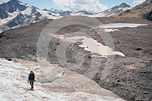 A mountaineer with a backpack walks in crampons walking along a dusty glacier with sidewalks in the hands between cracks