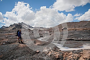A mountaineer with a backpack walks in crampons walking along a dusty glacier with sidewalks in the hands between cracks