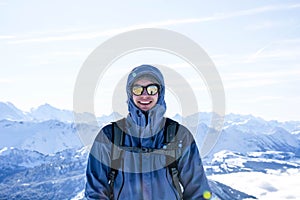 mountaineer backpacker smiling at the summit against blue snowy mountain layers in winter. sunny, blue sky