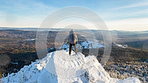 The mountaineer climbed the mountain top, man hiker standing at the peak of rock covered with ice and snow, view from