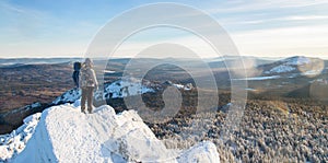 The mountaineer climbed the mountain top, man hiker standing at the peak of rock covered with ice and snow, view from