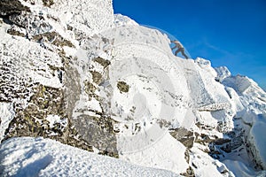 The mountaineer climbing the mountain top covered with ice and snow, man hiker going at the peak of rock. Winter season.