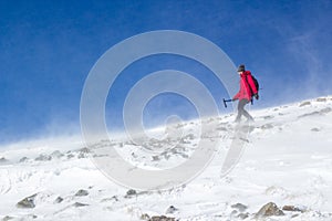 Mountaineer girl hiking in a snowed mountaind with hard wind
