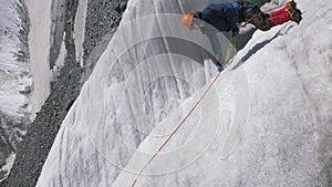 Mountaineer man in crampons is using ascender on fixed rope on steep slope in mountains. Vertical video