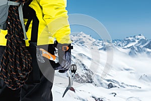 A mountaineer man holds an ice ax high in the mountains covered with snow. Close-up from behind. outdoor extreme outdoor