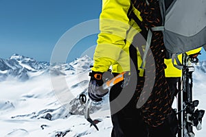 A mountaineer man holds an ice ax high in the mountains covered with snow. Close-up from behind. outdoor extreme outdoor