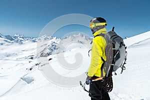 A mountaineer man holds an ice ax high in the mountains covered with snow. View from the back. outdoor extreme outdoor