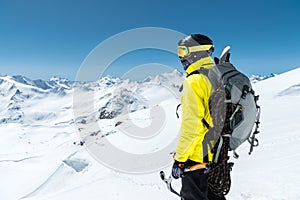 A mountaineer man holds an ice ax high in the mountains covered with snow. View from the back. outdoor extreme outdoor