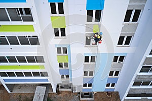 A mountaineer painter paints the wall of a multi-storey building at a height of. A can of multicolored paint is tied to the safety