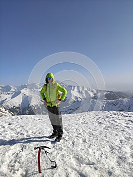 Mountaineer reaches the top of a snowy mountain in a sunny winter.