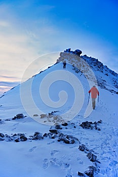 Mountaineer reaches the top of a snowy mountain in a sunny winter day