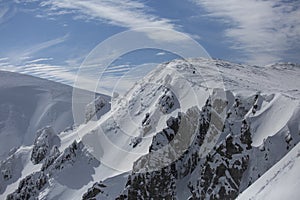 Mountaineer reaches the top of a snowy mountain in a sunny winter day