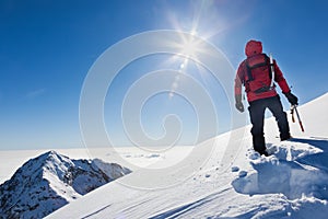 Mountaineer reaches the top of a snowy mountain in a sunny winter day.