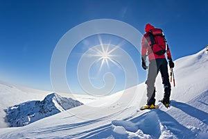 Mountaineer reaches the top of a snowy mountain in a sunny winter day.