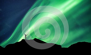 Mountaineer standing on top of mountain with Aurora Borealis glowing in the night sky on arctic circle