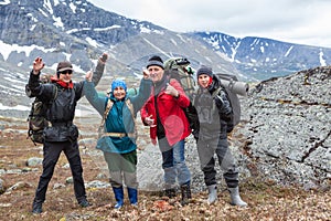 Mountaineers cheering and greeting with hands up, group of Caucasian hikers from one family hiking with backpacks in mountains