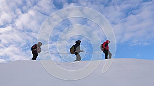 Mountaineers tied with rope follow each other along snowy ridge. team of travelers in winter go to top of the mountain