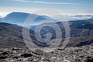 Mountainous landscape with slate terrain in the foreground, a gorge after it and mountains in the background with a sea of low photo