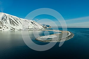The mountainous sea coast covered with snow in a sunny weather with an old beacon on the spit photo