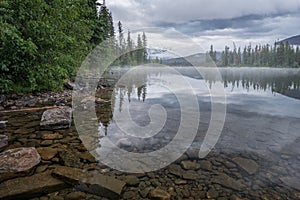 Mountains and clouds reflect in water surface of Pyramid Lake in Canadian Rockies. Misty, moody, rainy evening in Jasper National