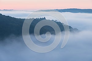 Mountains in fog at beautiful morning in autumn. Landscape with mountain valley, low clouds, forest, colorful sky , nature