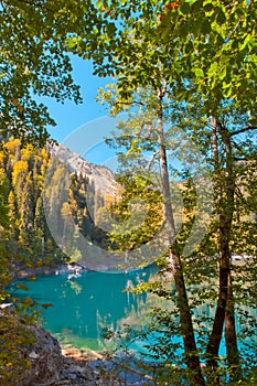 Mountains, green spruce trees and deciduous trees are reflected in the clear water of a mountain lake. Autumn