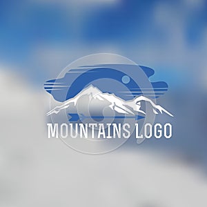 Mountains lodo on blurred background. Emblem with stylized mountain landscape photo