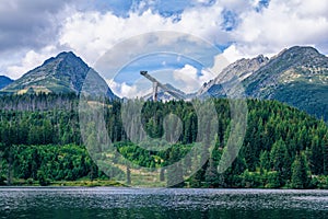 Mountains, lush forest, ski jumping tower and white clouds on blue sky