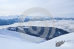 Mountains of main Caucasian Ridge covered with snow and forest and wooden fence