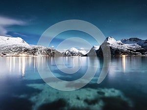 Mountains and reflections on water at night. Winter landscape. The sky with stars and clouds in motion. Nature as a background.