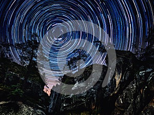 Mountains and trees on starry background with bright stars trail