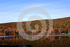 Mountainside filled with fall foliage reflecting off a lake in Allegany State Park, New York photo