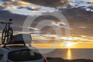 Mounted bicycle silhouette on the car roof with rising sun background. Dramatic sky at mediterranean sea dawn