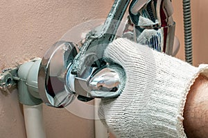 Mounting a faucet mixer, fixing a nut with an old wrench close-up. Worker`s hands in gloves