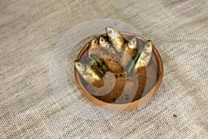 Mourala fish or indian carplet fish cooked in yellow gravy in teracotta bowl or earthen pot on beige jute textured background.