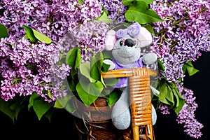 A mouse sits on a bicycle with a bouquet of lilacs close-up.