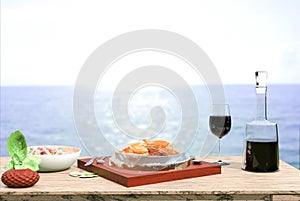 Moussaka dish accompanied by red wine from the island of crete, greek salad and fresh mint leaves on a defocused sea