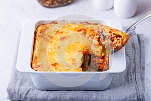 Moussaka with meat, eggplant, tomatoes, potatoes, bechamel sauce and cheese on a white plate. Traditional Greek dish. Close-up